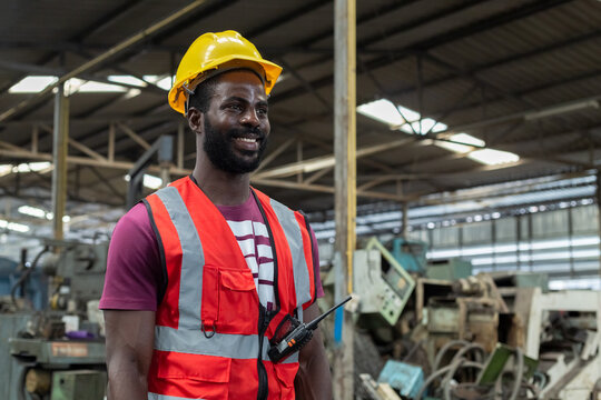 Portrait engineering male african american happy smiling workers wear yellow hard hat red uniform standing at factory industrial. Man technician machinery professional at workplace.