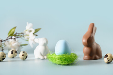 Easter yellow egg in green nest and chocolate rabbit in spring composition on blue background with copy space. Happy Easter greeting card.