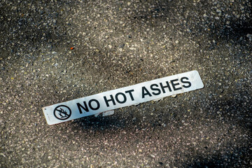 Sign that says no hot ashes on floor of barbeque location with white and black paint in late afternoon shadow