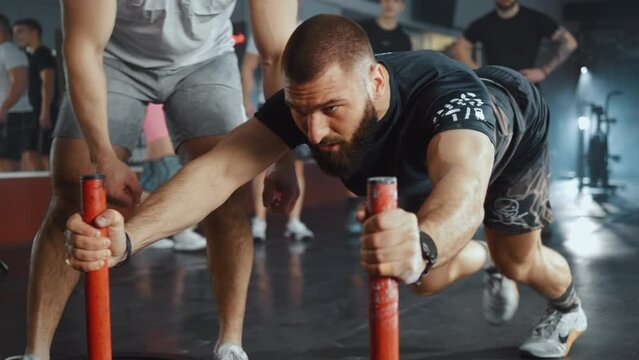 Concentrated muscular man pushing sled  during exercise slow motion. The group cheers and motivates the athlete who pushes heavy weight training sled in the gym.