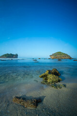 Obraz premium Tropical rocky beach with white sand and cliffs and blue sky with clouds on Sunny day. Summer tropical landscape, panoramic view. travel tourism wide panorama background concept. 