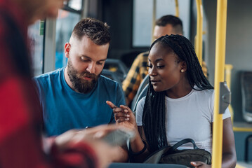 Multiracial friends talking and using a smartphone while riding a bus in the city