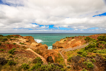 Naklejka premium Landscape in Port Campbell National Park, Victoria Australia with footpath over wooden steps and landings to the Grotto a sinkhole with eroded view to ocean and Bass Strait