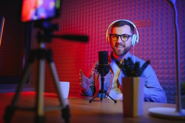 A video blogger records content in his studio. The host of the video blog is a young man who is...