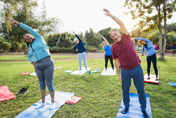 Multiracial senior people doing stretching workout exercises outdoor with city park in background - Healthy lifestyle and joyful elderly lifestyle concept - Focus on right man face