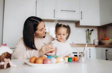 Obraz na płótnie Canvas Mom and daughter paint eggs with colors. Have fun. Happy family is preparing for Easter.