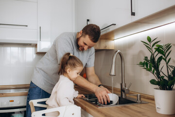 Father and daughter wash dishes in kitchen sink, Dad teaches kid wash dishes, helps child wash...
