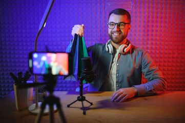 Naklejka na ściany i meble vlogger using smartphone to film podcast in studio. blogger with mobile phone, microphone and headphones filming video for social media broadcasting career.