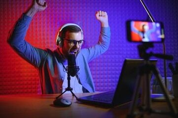 streamer is streaming online content,metaverse ar vr,gaming and esports concept.Happy man gamer wear headphone competition video game online with Laptop computer in colorful neon lights.