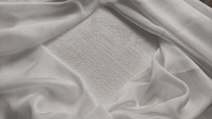 Abstract background with light delicate white fabric chiffon creating frame around square with white texture of paint or plaster. Beautiful curtains and hard rough texture of background