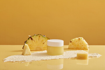 A jar of scrubs extracted from pineapple (Ananas comosus) decorated with pineapple slices and reflection under it. Ingredient to produce cosmetic