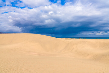 View of desert sand dunes against a moody cloudy blue sky. Maspalomas Dunes in Playa del Ingles, Maspalomas, Gran Canaria, Spain.