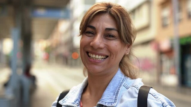 Mature latin woman smiling on camera while waiting at tram station in the city 