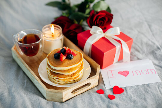 Holiday breakfast or brunch set served on gray bed with flowers, gift box and candle. Mother;s day, March 8, Valentines day concept