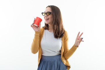 Brunette in a yellow sweater drinks coffee from a red cup.Young woman in stylish clothes on a white background