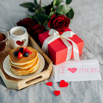 Mother's Morning breakfast on wooden tray with greeting card I love you mom, bouquqet of red roses, gift present box.