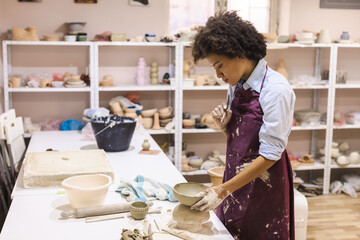 Fototapeta premium Creativ African American woman proudly stands in her pottery studio, skillfully decorate a clay cup with her hands. Her creative work is the result of years of practice as an artisan potter.