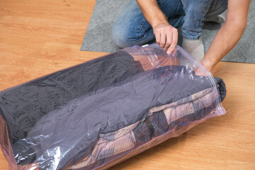 A man folds winter jackets and puts them in a vacuum bag for seasonal storage in the closet. Space...