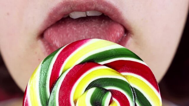Young woman licking a bright colorful lollipop candy with a tongue close up
