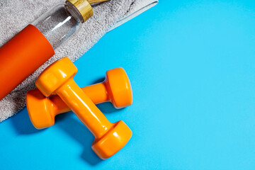 Two dumbbells with grey towel and bottle of water on turquoise background