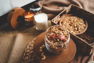 Fototapeta na wymiar Homemade granola in a glass jar, against the background of milk, candle and decor, good morning concept