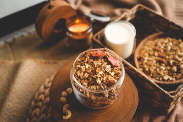 Homemade granola in a glass jar, against the background of milk, candle and decor, good morning...