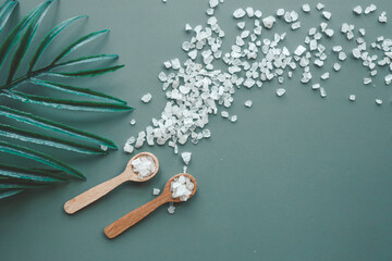 Sea salt on a green background in wooden spoons top view