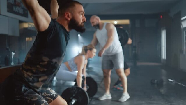 Athletic man lifting a barbell at gym during cross training. Personal trainer shows a group of people how to exercising  with a barbell in the gym. 