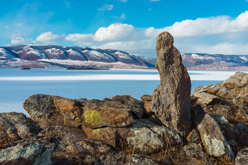 A stone standing upright against a blue sky, among rocky formations.Behind lake Baikal.