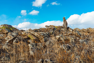A stone standing upright against a blue sky, among rocky formations.