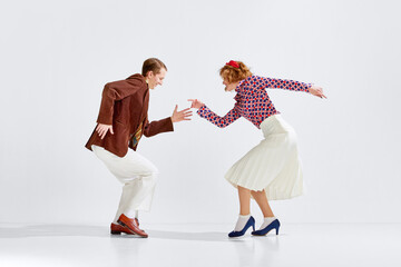 Old-school party. Young cheerful man and woman in stylish clothes dancing retro dance against grey...