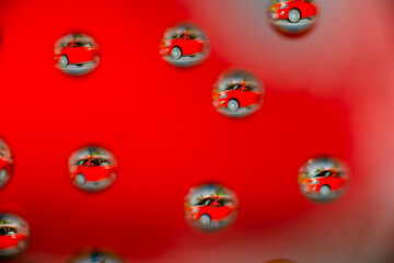 Image of a car reflected in water drops on red background.
