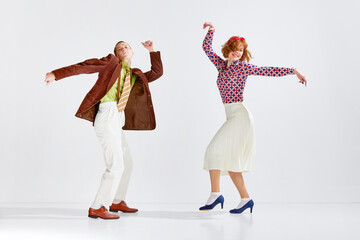 Young man and woman in stylish colorful clothes dancing retro dance against grey studio background....