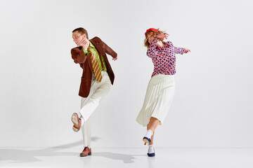 Boogie-woogie. Young man and woman in stylish clothes dancing retro dance against grey studio background. Concept of art, retro style, hobby, party, fun, movements, 60s, 70s culture