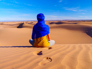 Woman with blue berber turban sitting in sahara desert and looking panoramic view