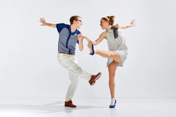 Fotobehang Dansschool Happy and delightful people. Young man and woman in stylish clothes dancing retro dance against grey studio background. Concept of art, retro style, hobby, party, fun, movements, 60s, 70s culture