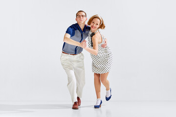 Young happy man and beautiful smiling woman in stylish clothes dancing retro dance against grey...