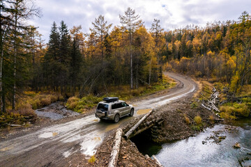 SUV on wooden bridge over small mountain river. Autumn forest.