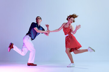 Active delightful young man and woman in colorful costumes dancing retro style dances against...