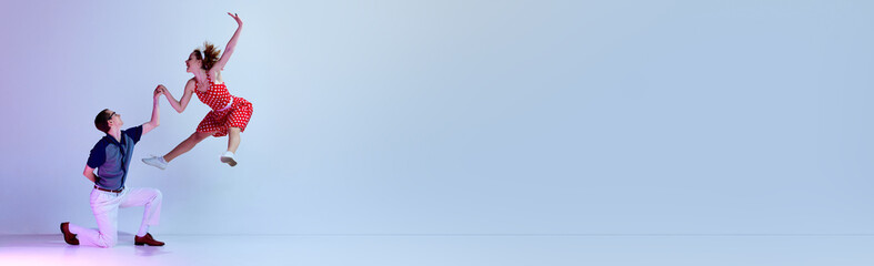 Beautiful young couple, man and woman in stylish clothes dancing retro style dances over gradient blue purple studio background. Art, retro style, hobby, party, fun, 60s, 70s culture concept. Banner