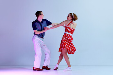 Beautiful young couple, man and woman in stylish costumes dancing retro dances against gradient...
