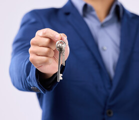 Realtor, keys and studio closeup of hands for man, new home or property by gray background. Businessman, real estate agent and entrepreneur for buying building, apartment and goals with key at job