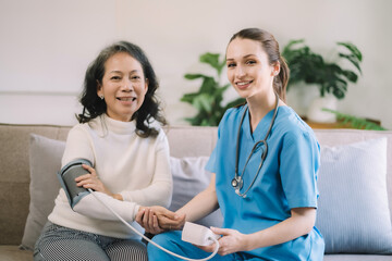 Female doctor checking old woman blood pressure at clinic and filling patient history in the morning.