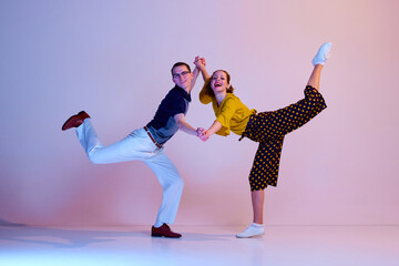 Happy emotional young couple, man and woman in stylish clothes dancing retro dance against gradient...
