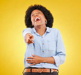 Pointing, laughing and fun with a black woman in studio on a yellow background enjoying a funny joke. Comic, comedy and laughter with an attractive young female feeling silly, goofy or playful