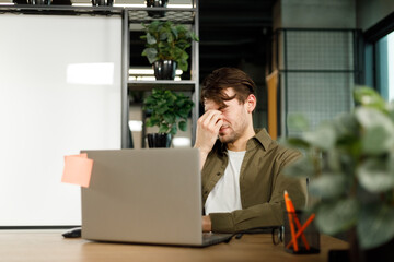 Stressed tired man suffering from headache in front of computer holding his glasses - Worried male entrepreneur thinking about problems and project deadline feeling exhausted