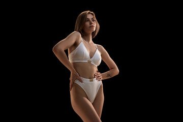 Young slim woman wearing white cotton lingerie posing over dark background. Concept of natural beauty, body and skin care, health, spa, cosmetics, ad