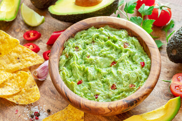 Guacamole, guacamole ingredients and chips on wooden background.
