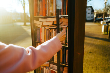 Young caucasian woman choosing books at free open public library at city park for book sharing...