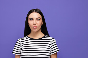 Fototapeta premium Beautiful young woman blowing kiss on purple background